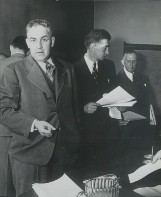 Photograph of Assemblyman John Ostrander, Paul Schaefer, and Sanford D. Stockman standing in suits in front of a table during the two day Ostrander Amendment public hearings at the American Museum of Natural History in New York City on January 20-21, 1950.