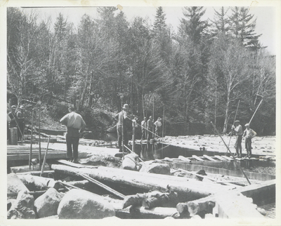 River drivers standing on docks on Henderson Lake, NY surrounded by logs, May 1931. They are waiting for the wind to change from the south to the west to blow the logs across the lake to a dam which will send them down the Henderson River to the lumber mills on the Hudson River. Bill Gluesing and Paul Schaefer took this on a trip to photograph Indian Pass from Henderson Lake.