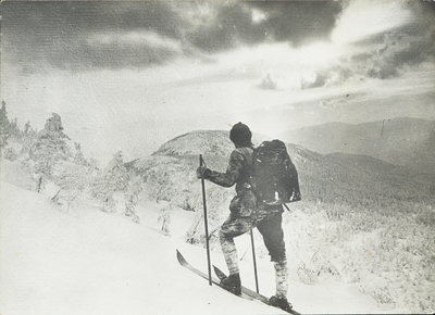 Apperson skis up a mountain, pausing to take in the vista, circa 1910.