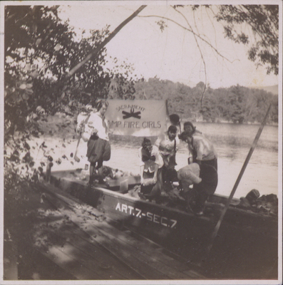 Seven Campfire Girls holding a flag and rocks standing in John S. Apperson Jr.'s boat ART.7.-SEC.7., which is loaded with rocks for riprapping. The boat is named after Article VII Section VII of the New York State Constitution, more commonly referred to as the Forever Wild clause.
