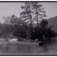 John S. Apperson Jr. in a bathing suit throwing a rock from a boat toward an island for riprapping in Lake George, NY, 1910.