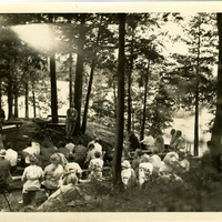 Crowd of attendees listening to John S. Apperson Jr. and one other man lecturing in front of maps of the Adirondacks at his camp Chilhowie on Lake George, NY at a Forest Preserve Association of New York State meeting during the summer of 1938.