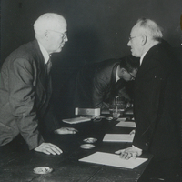 Photograph of John S. Apperson, Jr. leaning over a table to speak to Chauncey Hammond, a member of the Senate Judiciary Committee of New York State, during the two day Ostrander Amendment public hearings at the American Museum of Natural History in New York City on January 20-21, 1950.