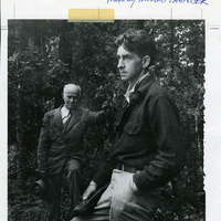 Photo of Paul Schaefer with his mentor John S. Apperson Jr. standing outdoors in the Adirondacks. Schaefer is dressed in a plaid button up shirt and looks off camera, while Apperson stands behind donning a suit and holding a hat. Photo taken by noted conservationists Howard Zanhiser.