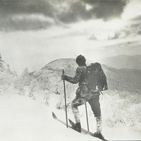 Apperson skis up a mountain, pausing to take in the vista, circa 1910.